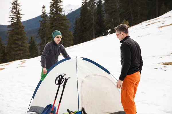 Two hikers in winter mountains installing tent