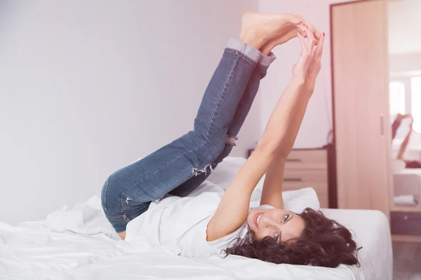 Brunette long hair woman in blue jeans lies on white bed linen