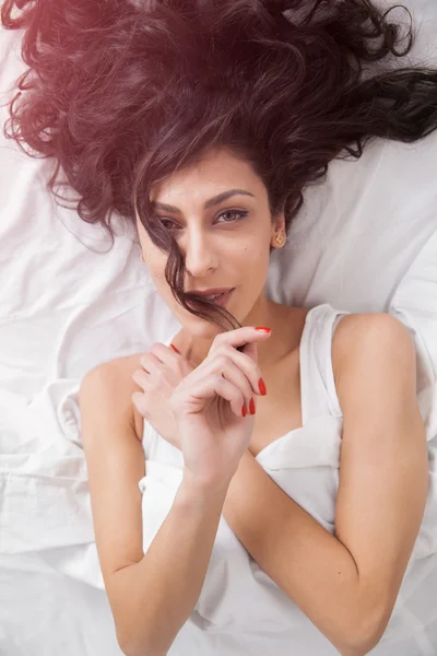 Brunette long hair woman lies on white bed linen