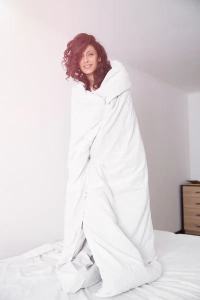 Brunette long hair woman covered by white duvet on hite bed