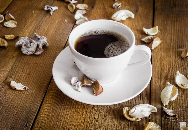 Cup of coffee on wooden background, decorated dried aromatic parts of plants
