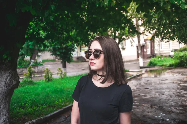 Beautiful girl in dark glasses and black shirt in the city near the tree
