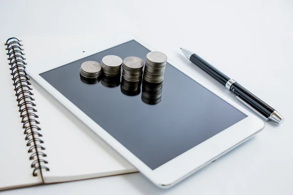 Coins set up in  graph, line chart on tablet and notebook. Put a pen beside tablet. business concept for \