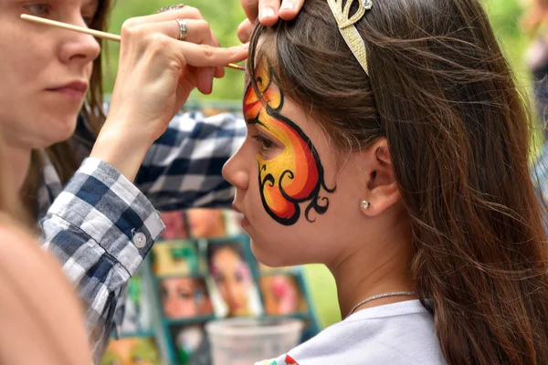 NOVOSIBIRSK, RUSSIA - JUNE 26, 2016: Master draws paints patterns on the girl\'s face in a city park