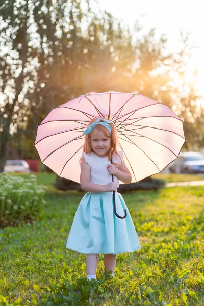 Adorable little girl in the park at sunset with umbrella