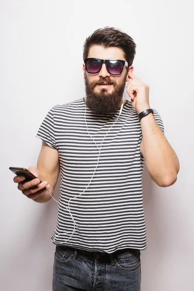 Happy Hipster with beard wearing  shirt and sunglasses enjoying music against white background
