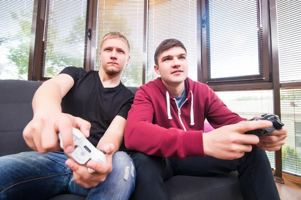 Two handsome young men playing video games while sitting on sofa