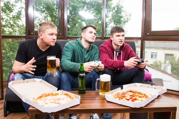 Smiling male friends playing video games, drink beer and have fun at home