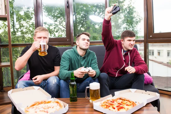 Smiling male friends playing video games, drink beer and have fun at home