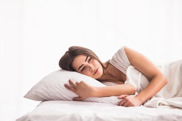 Sleeping woman is lying in bed with her head on the pillow and hands under it.