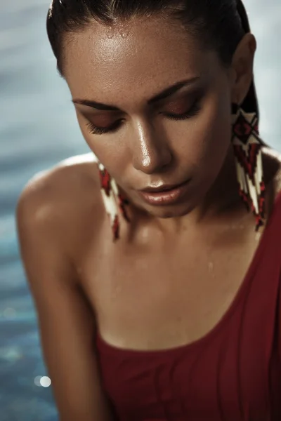 Portrait of a beautiful sun-tanned girl in a swimsuit with wet sleeked hair, closed eyes and big ethnic earrings