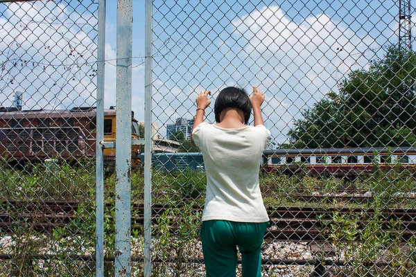 Asian girl sad alone hand hold jail at Railroad,railway station