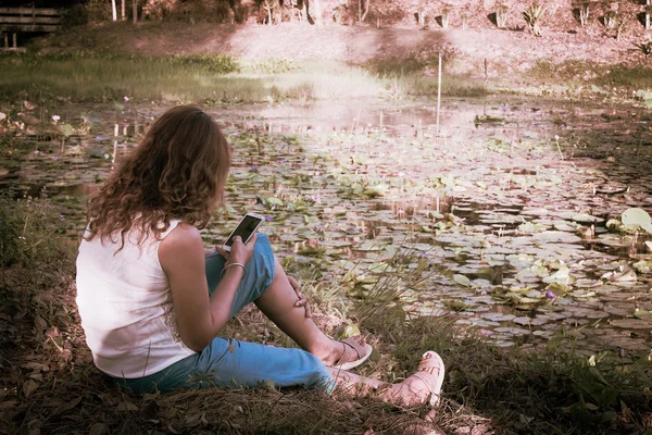 Vintage of asian woman sitting at river and play smart phone