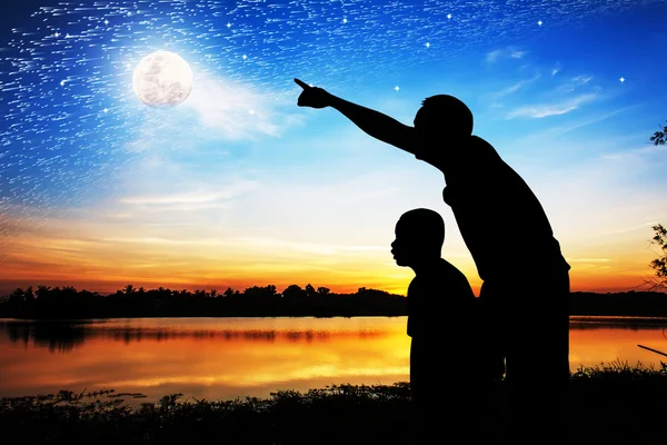 Silhouette of father use hand point his son look at meteor showe