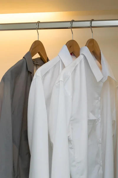 Row of white and grey shirts hanging on coat hanger in white wardrobe