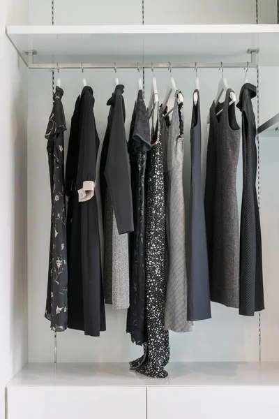Modern closet with row of black dress hanging on coat hanger in wardrobe.