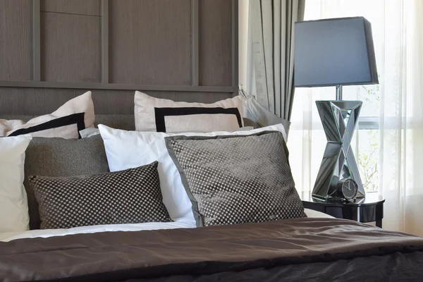 Stylish bedroom interior design with black patterned pillows on bed and decorative table lamp.