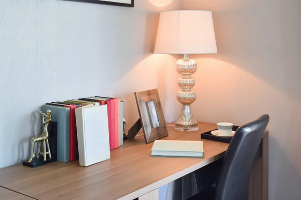 Wooden table with reading lamp and books in modern working room