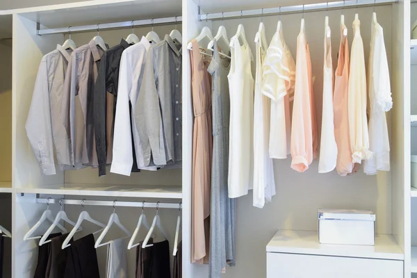Row of white dress and shirts hanging in white wardrobe