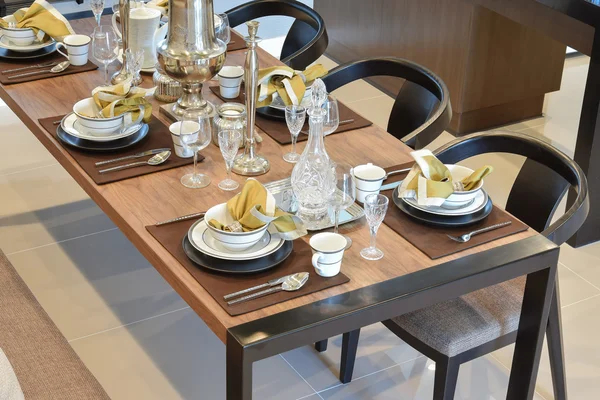 Dining wooden table and comfortable chairs in modern home with elegant table setting