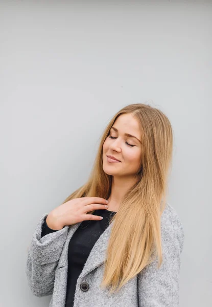 Blonde young woman standing behind the wall and posing ti camera