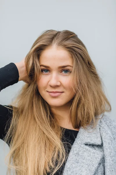 Blonde young woman standing behind the wall and posing ti camera