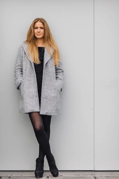 Blonde young woman standing behind the wall and posing ti camera