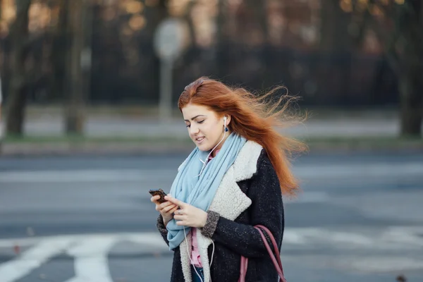 Red-haired girl walking on the street and listen music on her phone