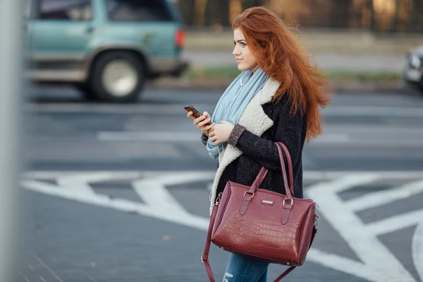 Red-haired girl walking on the street and listen music on her phone