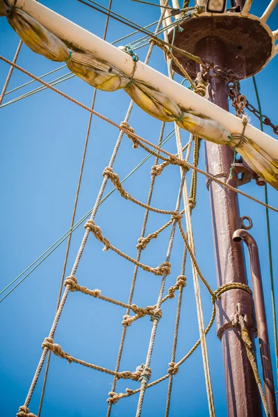 The mast of old ship with sail and ladder made of rope.