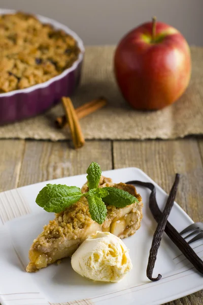 Apple pie with ice cream, decorated with vanilla, mint and cinnamon on wooden background.