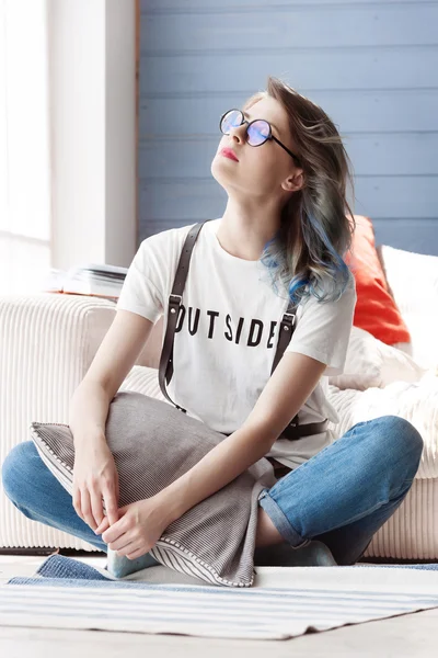 Cheerful young girl with fancy blue hair and round glasses.