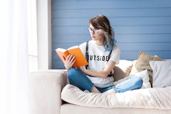 Young smart female student studying diligently at home near large window. Balcony, sofa, soft pillows.