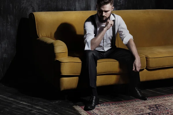 A young handsome bearded man sitting on orange couch in a dark room