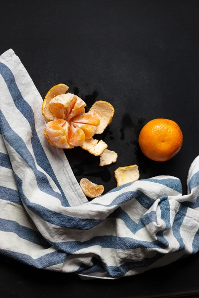 Two tangerines are lying on the black table with a striped linen towel.