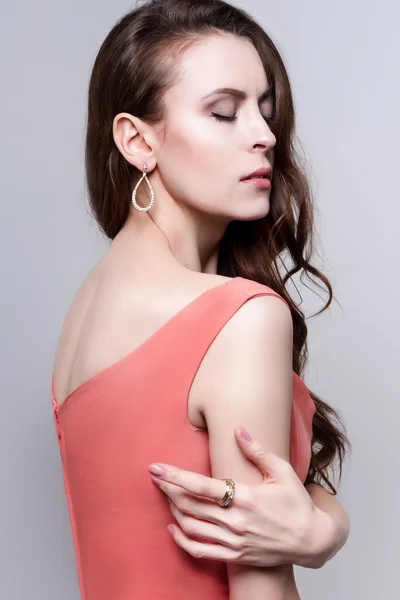 Attractive woman in coral dress and golden jewelry