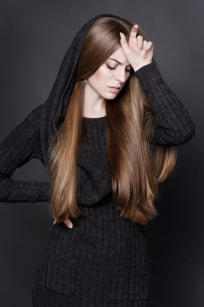 Young attractive woman with long, gorgeous dark blond hair. She is dressed in warm gray knit dress