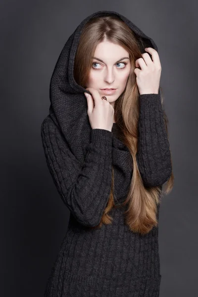 Young attractive woman with long, gorgeous dark blond hair. She is dressed in warm gray knit dress with a hood.