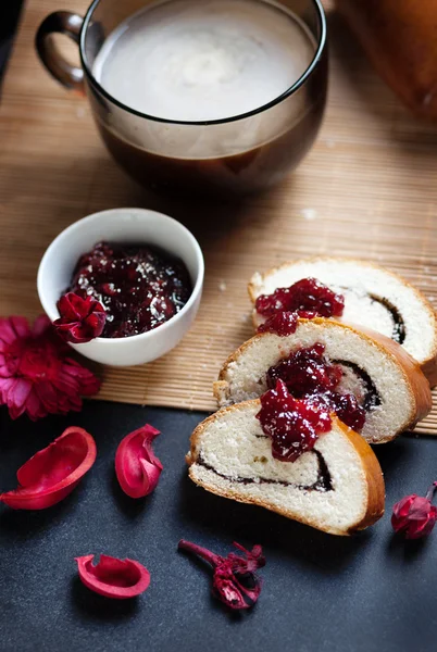 Slices of butter poppy roll, served with cherry jam and large glass cup with hot coffee