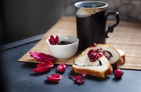 Slices of butter poppy roll, served with cherry jam and large ceramic cup with hot drink