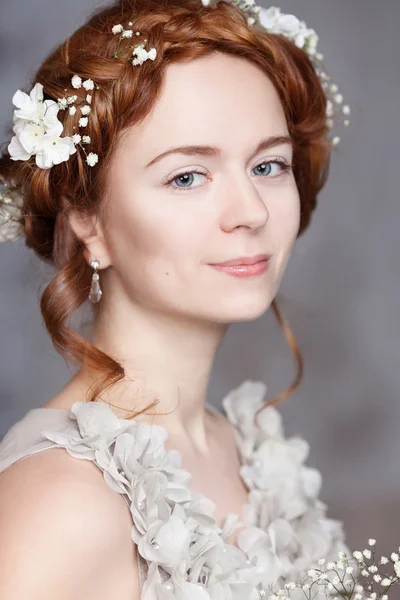 Portrait of beautiful red-haired bride. She has a perfect pale skin with delicate blush. White flowers in her hair.