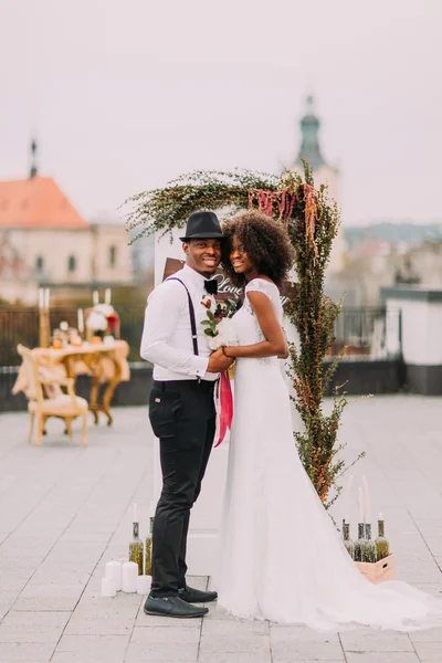 Cheerful black bride and groom holding hands on the wedding ceremony on rooftop