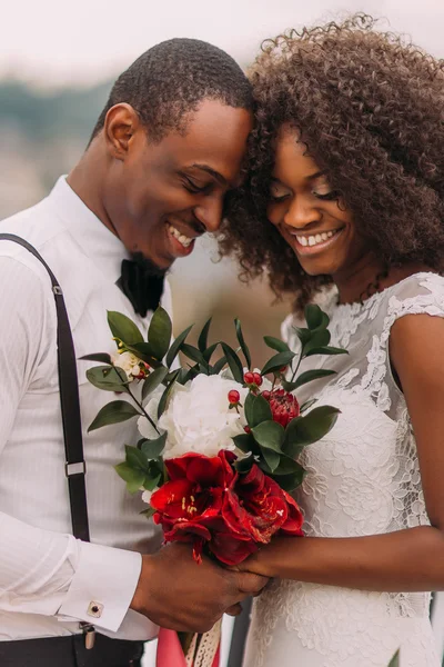 African wedding couple softly smiling with eyes closed with bouquet in hands