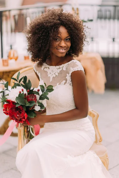 Charming african bride with wedding bouquet in hands cheerfully smiling to the camera
