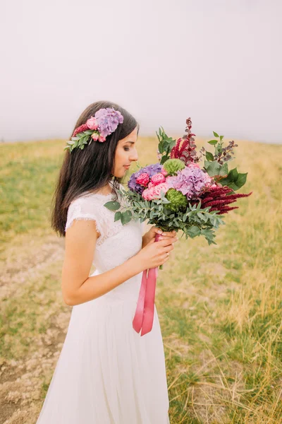 Brunette bride with bouquet in hands on the field. Fog background