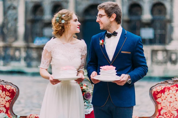 Happy wedding couple lovingly look at each other with pieces of wedding cakes in hands