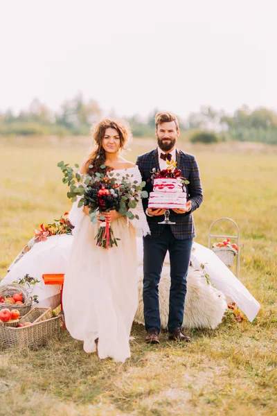 Wedding couple smiling with bouquet and cake at the field