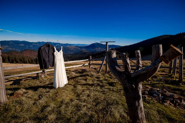 Wedding dress and  grooms suit hanging on hanger. Amazing mountain landscape  background