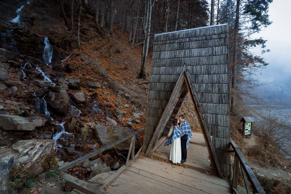 Wedding couple softly kiss on the wooden bridge. Misty day in mountains