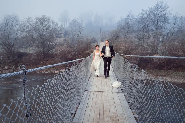 Cheerful newlyweds walking and laughing on the wooden bridge. Honeymoon at mountains